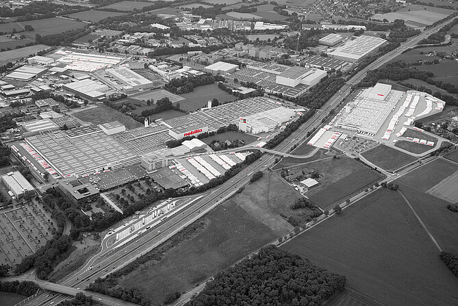 Luftaufnahme eines ausgedehnten Industriekomplexes mit zahlreichen Lagerhäusern und Fabriken, umgeben von grünen Feldern und durchzogen von Straßen.